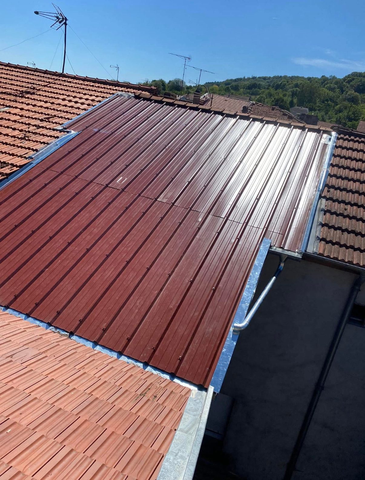 Toiture en bac acier rouge entre deux toits de tuiles